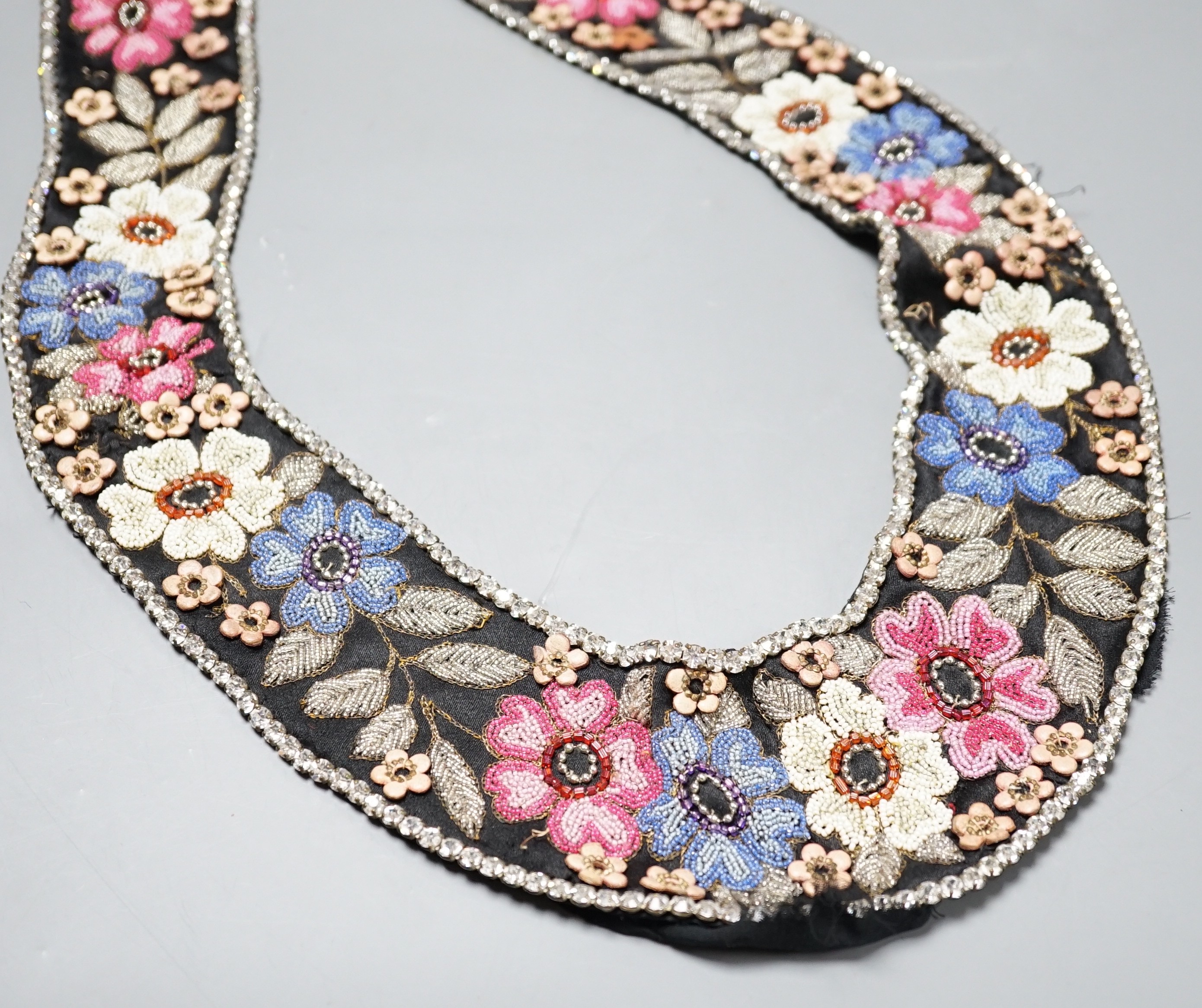 A 1920’s-30’s French beaded collar, the beads embroidered as flowers and leaves with leather applice flowers and diamanté edging, 115 cms long